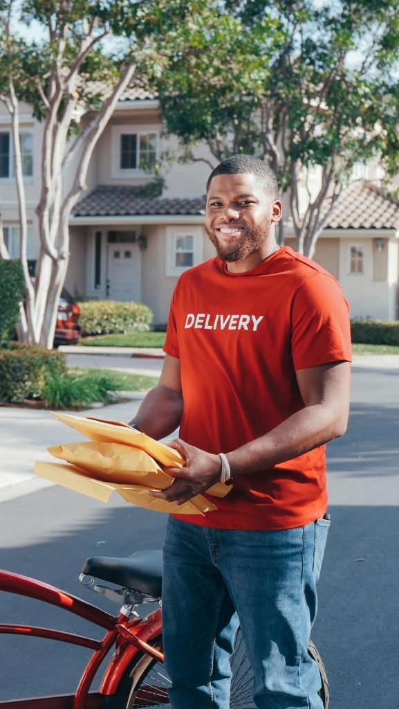 A friendly delivery man holding parcels outdoors near suburban homes, ready for safe delivery.